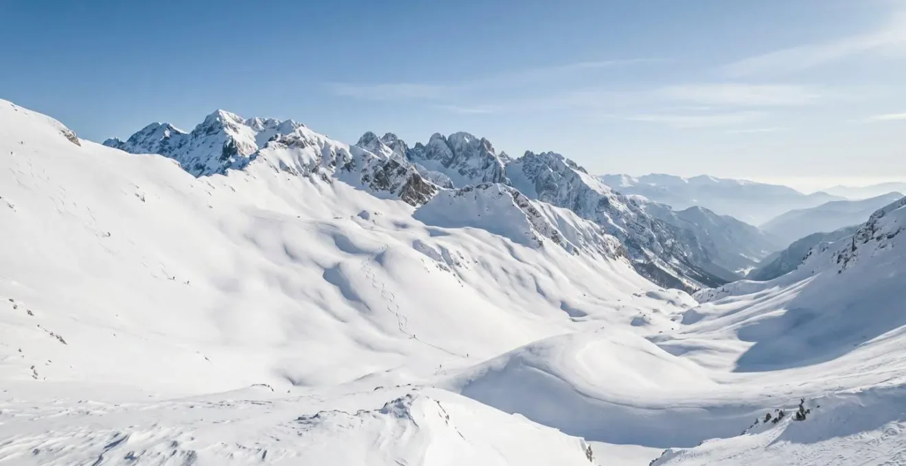 Panoramic view of snowy mountain slopes with skiers descending through pristine alpine terrain