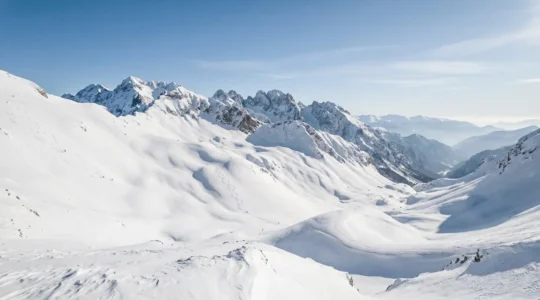 Panoramic view of snowy mountain slopes with skiers descending through pristine alpine terrain