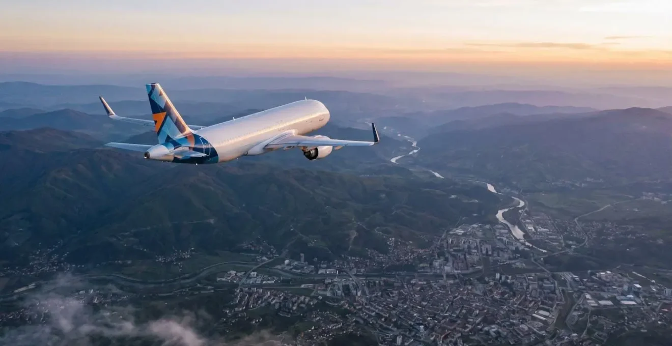 Minimalist aerial view of a modern budget airline aircraft flying over mountainous Balkan landscape with scattered clouds and urban center below