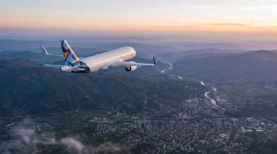 Minimalist aerial view of a modern budget airline aircraft flying over mountainous Balkan landscape with scattered clouds and urban center below