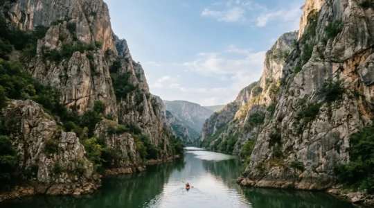 Dramatic limestone cliffs towering over emerald Treska River waters in Matka Canyon with kayaker exploring peaceful natural gorge near Skopje