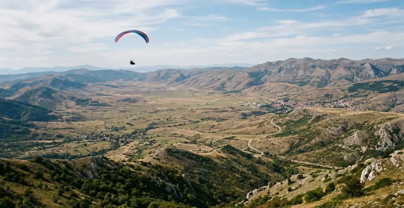 Paraglider soaring above the Kruševo valley with mountain peaks and thermal air columns visible in wide scenic landscape