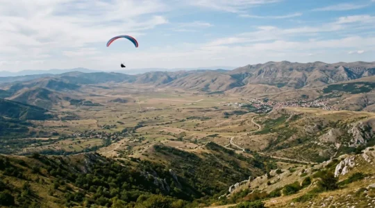 Paraglider soaring above the Kruševo valley with mountain peaks and thermal air columns visible in wide scenic landscape